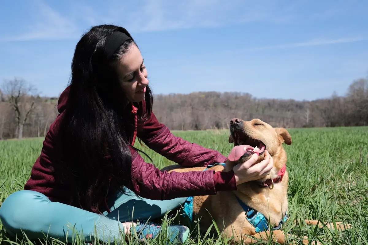 Abby sentada en un campo de hierba, sonriendo mientras rasca detrás de las orejas a su perro Anderson.